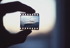 a person holding up a polaroid with a ship in the background on it's side