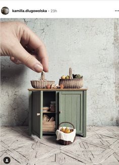 a hand reaching for food on top of a green cabinet next to a basket filled with fruit