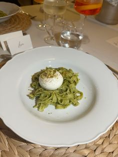 a white plate topped with pasta and an egg on top of it next to a glass of wine