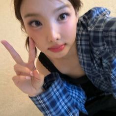 a young woman making the peace sign with her hand while wearing a blue and white checkered shirt