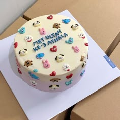 a white cake with lots of small teddy bears on it's icing sitting on top of a cardboard box