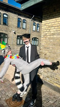 a man in a suit and tie is being carried by a woman dressed as a raccoon