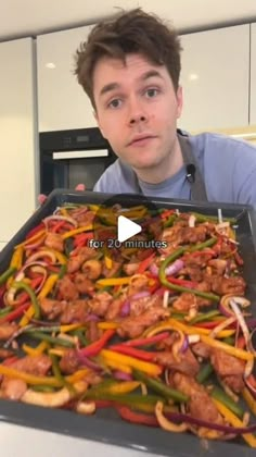 a man holding a pan full of chicken and peppers