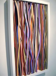 an art piece is displayed in a white frame with multicolored ribbons on it