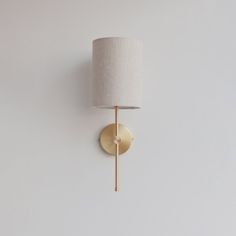 a wall light with a white shade on it's side and a gold arm