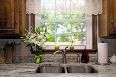 a kitchen sink under a window next to a counter top with an apple vase on it