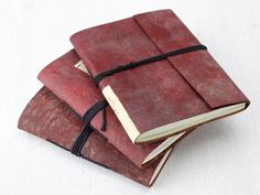 three red leather notebooks stacked on top of each other with black string attached to them