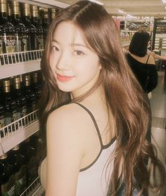 a young woman standing in front of a rack of wine bottles at a grocery store