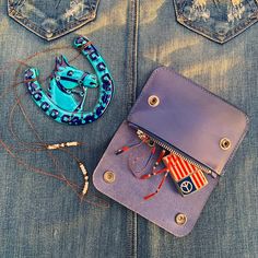 a blue purse sitting on top of a pair of jeans next to a small necklace