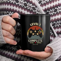 a person holding a black coffee mug with a video game controller on it's side