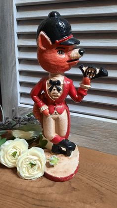 a figurine of a fox holding a baseball bat on a table next to flowers