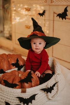 a baby wearing a witches hat sitting in a basket filled with pumpkins