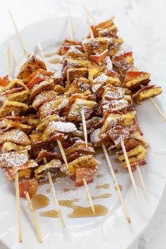 bacon and cheese skewers on a white plate with syrup drizzled over them