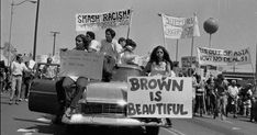 a group of people riding on the back of a car down a street holding signs