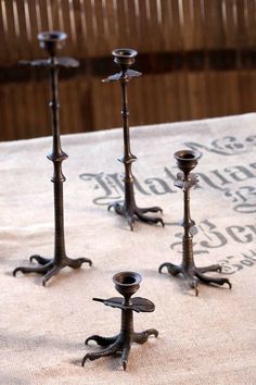 four metal candlesticks sitting on top of a white tablecloth covered floor next to each other