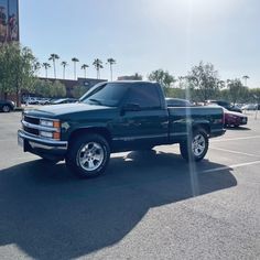 a green truck parked in a parking lot next to other cars and palm tree's