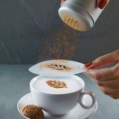 a person sprinkling coffee into a white cup on top of a saucer