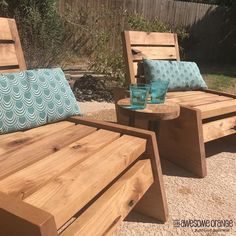 two wooden lounge chairs sitting next to each other on top of a gravel ground near a fence