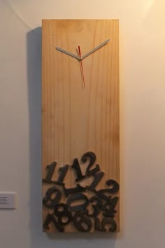 a clock made out of wooden letters and numbers on a white wall with a red light in the background