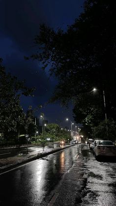 cars are parked on the side of the road in the rain at night with street lights