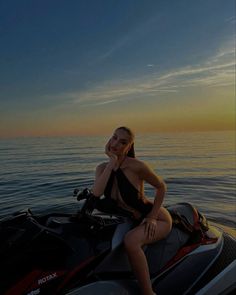 a woman sitting on the back of a jet ski in the ocean at sunset or dawn