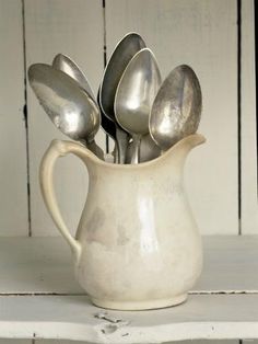 a white pitcher filled with silver spoons on top of a table