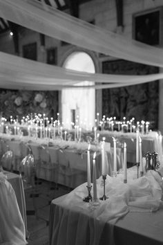 many lit candles are on the tables in this room with white linens and tablecloths