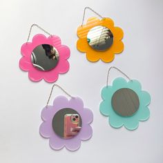 four flower shaped mirrors hanging from chains on a white surface with a hand holding a cell phone