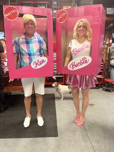 two people are standing in front of pink boxes with barbie dolls on them and one person is holding a dog