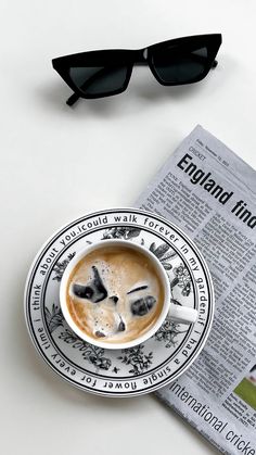 a cup of coffee on top of a newspaper next to sunglasses