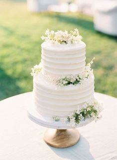 a white wedding cake sitting on top of a wooden table next to a grass covered field