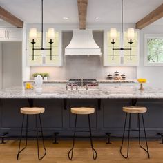 a kitchen with three stools in front of an island and two lights hanging from the ceiling