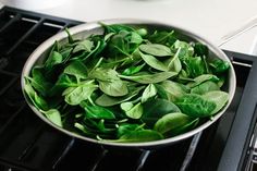 a pan filled with green leaves on top of an oven