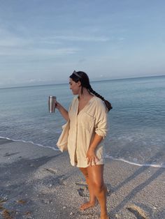 a woman standing on the beach holding a cup