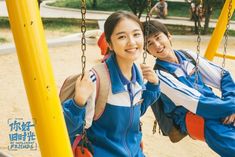 two young women sitting on swings at a playground together, one smiling and the other looking into the camera