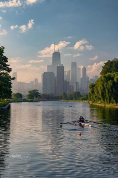 two rowers paddling down the river in front of large city buildings on a sunny day