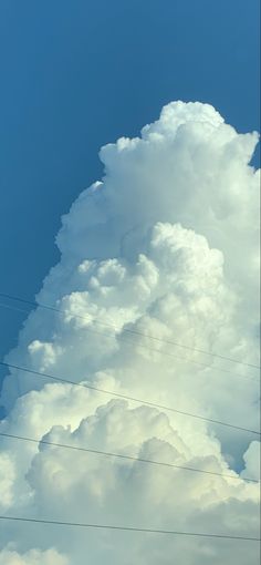 an airplane flying high in the sky above power lines and telephone wires under a cloudy blue sky