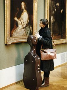 a woman standing next to a large painting in an art museum with a guitar on the floor