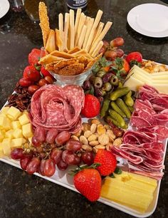 an assortment of cheeses, meats, and fruits on a platter with crackers