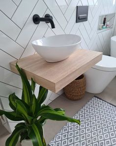 An amazing light wood floating shelf is mounted to a white herringbone bathroom tile. The shelf is fitted with a white vessel sink accompanied by a black wall-mounted faucet. A cute white and gray diamond bath mat is laid under the sink over greige floor tiles...   Image: renovating_salisbury