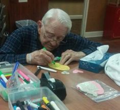 an older man sitting at a table with lots of crafting supplies on top of it