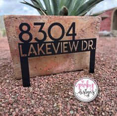 a sign that is on the ground in front of a plant and some gravel with a sky background