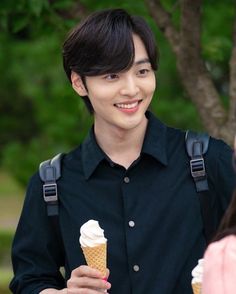 a young man holding an ice cream cone in his hand while standing next to a woman