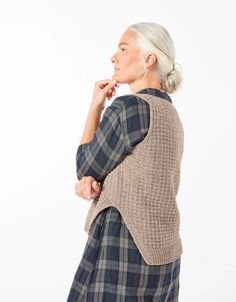 an older woman with white hair wearing a blue and gray plaid sweater, looking off to the side