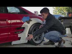 a man working on a car tire in front of a red car with blue paint