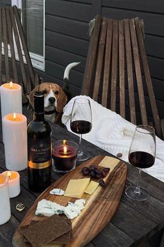 a dog sitting at a table with some wine and cheese on it next to candles