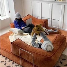 a person sitting on an orange couch with a stuffed animal in front of them, using a laptop