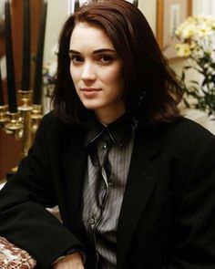 a woman wearing a suit and tie sitting at a table with flowers in the background