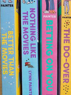 there are four books on the shelf together in different colors and designs, one is pink, blue, yellow, and green