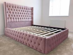 a bed that is made up in some kind of pink color and has buttons on the headboard